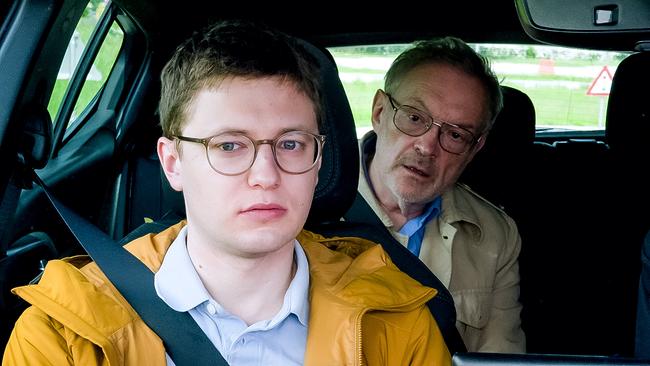 © ORF/KGP Filmproduktion Fahrlehrer Florian mit Brille und gelber Jacke sitzt angeschnallt im Auto, während Josef Hader als Fahrprüfer mit Brille sich von der Rückbank zu ihm nach vorne beugt.