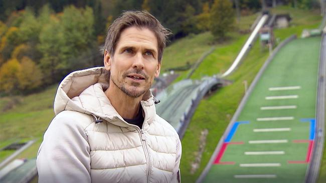 Felix Gottwald in einer hellen Steppjacke vor einer Sommer-Skisprunganlage in einer herbstlichen Berglandschaft.