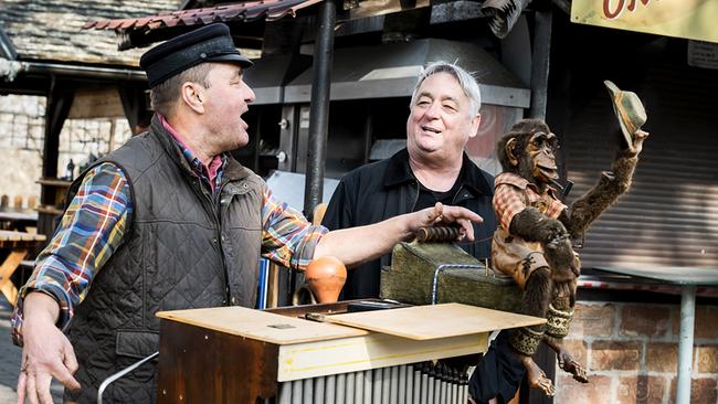 Andreas Vitásek steht im Prater neben einem Orgelspieler an einer historischen Drehorgel, während eine bekleidete Affenfigur darauf platziert ist.