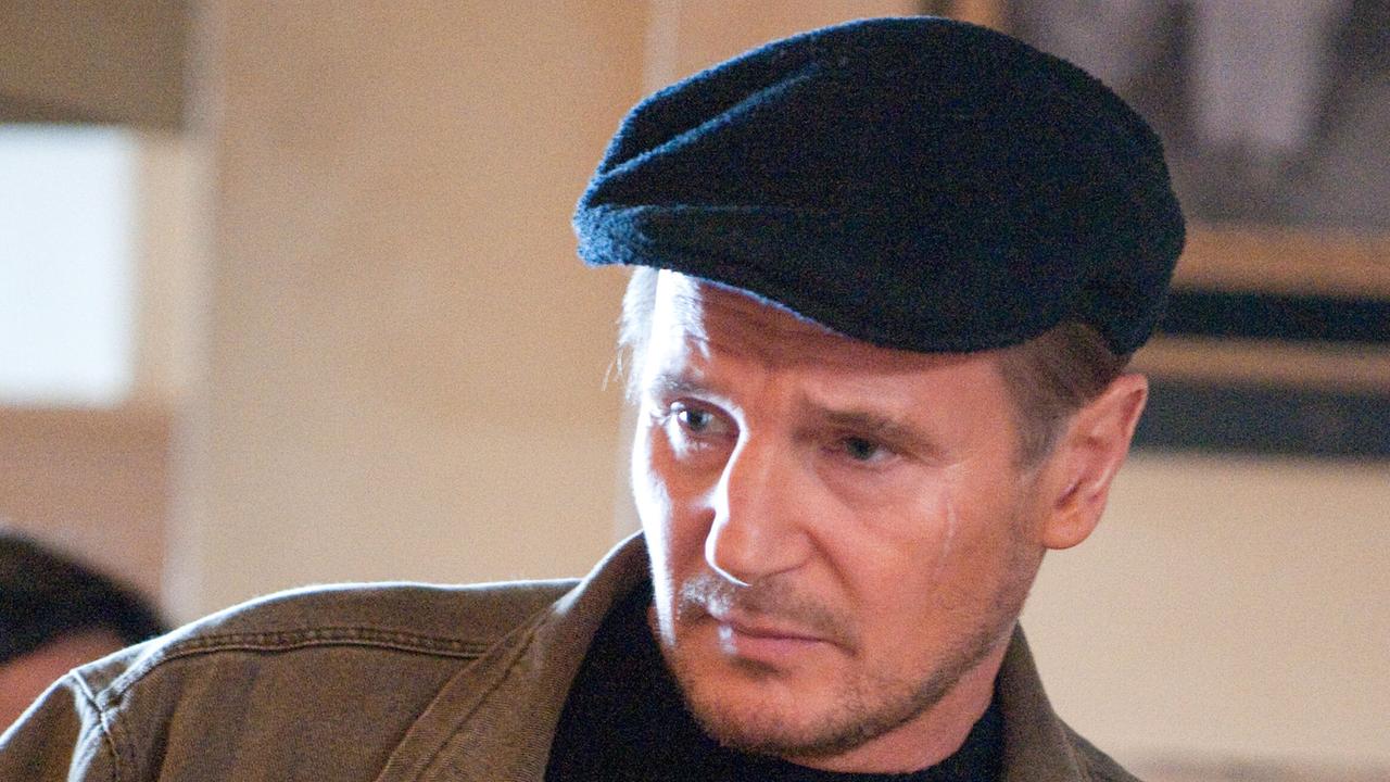 Liam Neeson als Damon Pennington, der eine dunkelblaue Schirmmütze und eine olivgrüne Jacke trägt