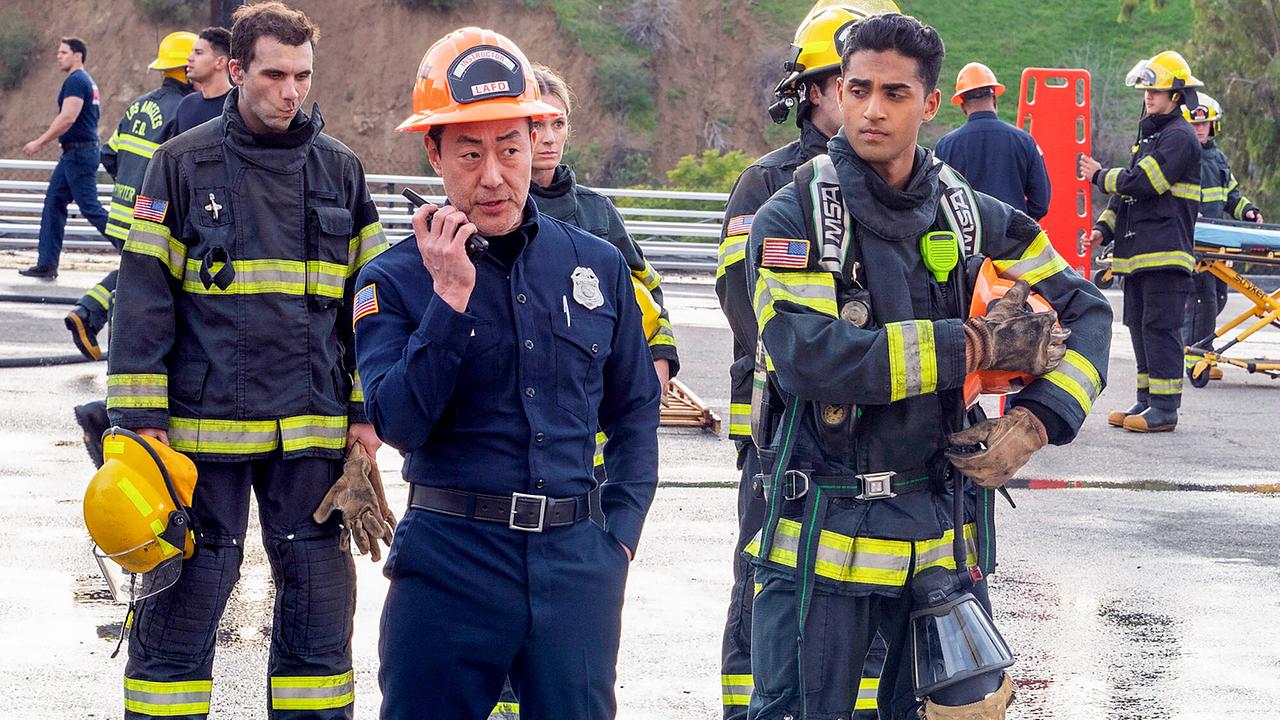 © ORF/PRO7/© 2023 20th Television/Jack Zeman Mehrere Feuerwehrmänner stehen nach einem Einsatz auf der Straße, Chimney spricht in sein Walkie Talkie, Ravi schaut ihn prüfend von der Seite an