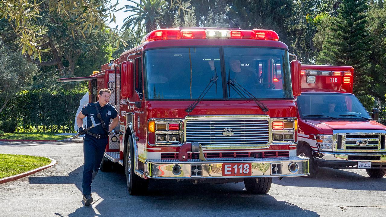 Zwei Feuerwehrwagen stehen in der Einfahrt im Vorgarten eines Anwesens, mit Warnlicht, Buck läuft in leichter Montur mit einer Hacke vorbei
