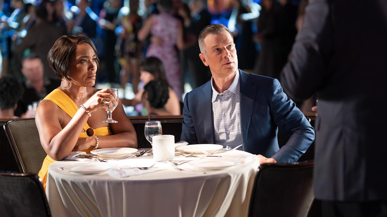 Athena Grant und Bobby Nash sitzen am Tisch beim Abendessen auf ihrer Kreuzfahrt, erstaunt schauen sie jemand an, der sich ihrem Tisch genährert hat