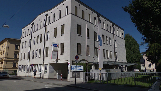 Außenansicht AMS-Gebäude mit Fahnen davor und Straße.