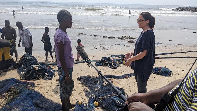 Lisa Gadenstätter interviewt eine Fischerin auf einem Strand in Ghana und spricht mit ihr darüber, wie sehr der Modemüll die Fischerei beeinträchtigt.