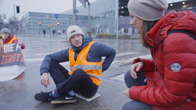 Lisa Gadenstätter kniet Aktivist Leon Ranz bei einer Klebe-Aktion auf dem Wiener Praterstern und spricht mit ihm über seine Beweggründe.