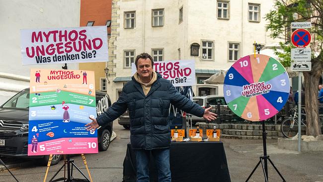 Hanno leitet das Spiel Mythos ungesund ein. Er steht auf einem Marktplatz, hinter ihm ein Spielrad 