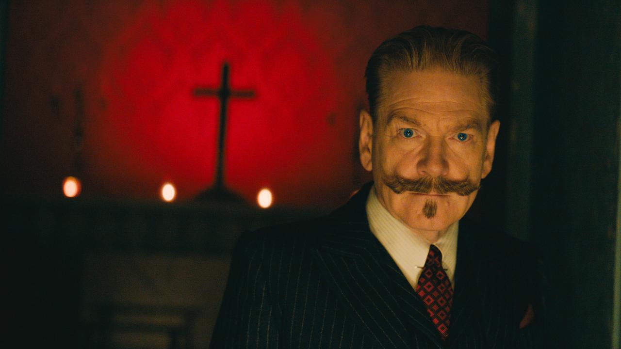 Kenneth Branagh als Hercule Poirot - in einem dunklen Raum ist sein Gesicht beleuchtet, hinter ihm ein Kreuz vor einer rot tapezierten Wand