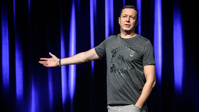 Alex Kristan gestikuliert auf der Bühne vor blauem Vorhang bei seinem Programm "50 Shades of Schmäh"