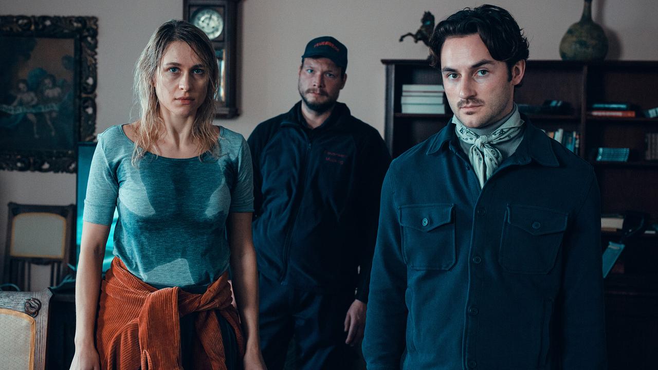 © ORF/Allegro Film/Stefan Robitsch Radlerin, Andreas und Georg stehen mit angespannten Mienen in einem Wohnzimmer.