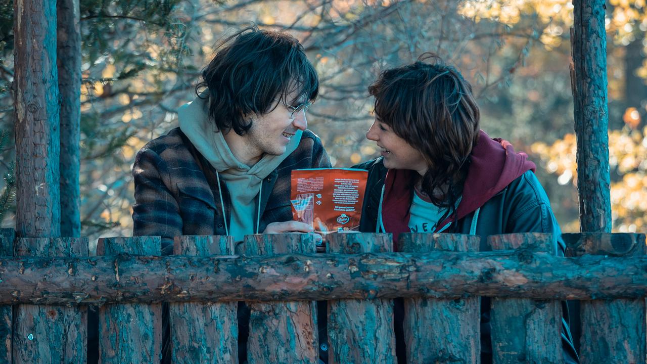 © ORF/Allegro Film/Anjeza Cikopano Jakob und Marie unterhalten sich lächelnd in einem hölzernen Unterstand im Wald.