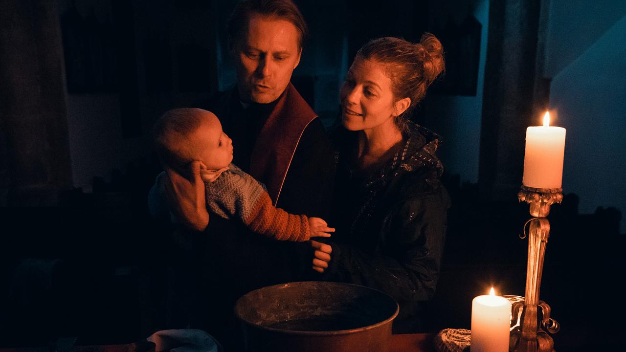 © ORF/Allegro Film/Anjeza Cikopano Bei Kerzenlicht hält Matias ein Baby über eine Schale, während Elisabeth danebensteht.