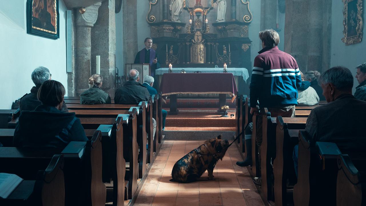 © ORF/Allegro Film/Anjeza Cikopano Während eines Gottesdienstes steht Klaus mit Schwein Schnitzi im Mittelgang einer kleinen Kirche.