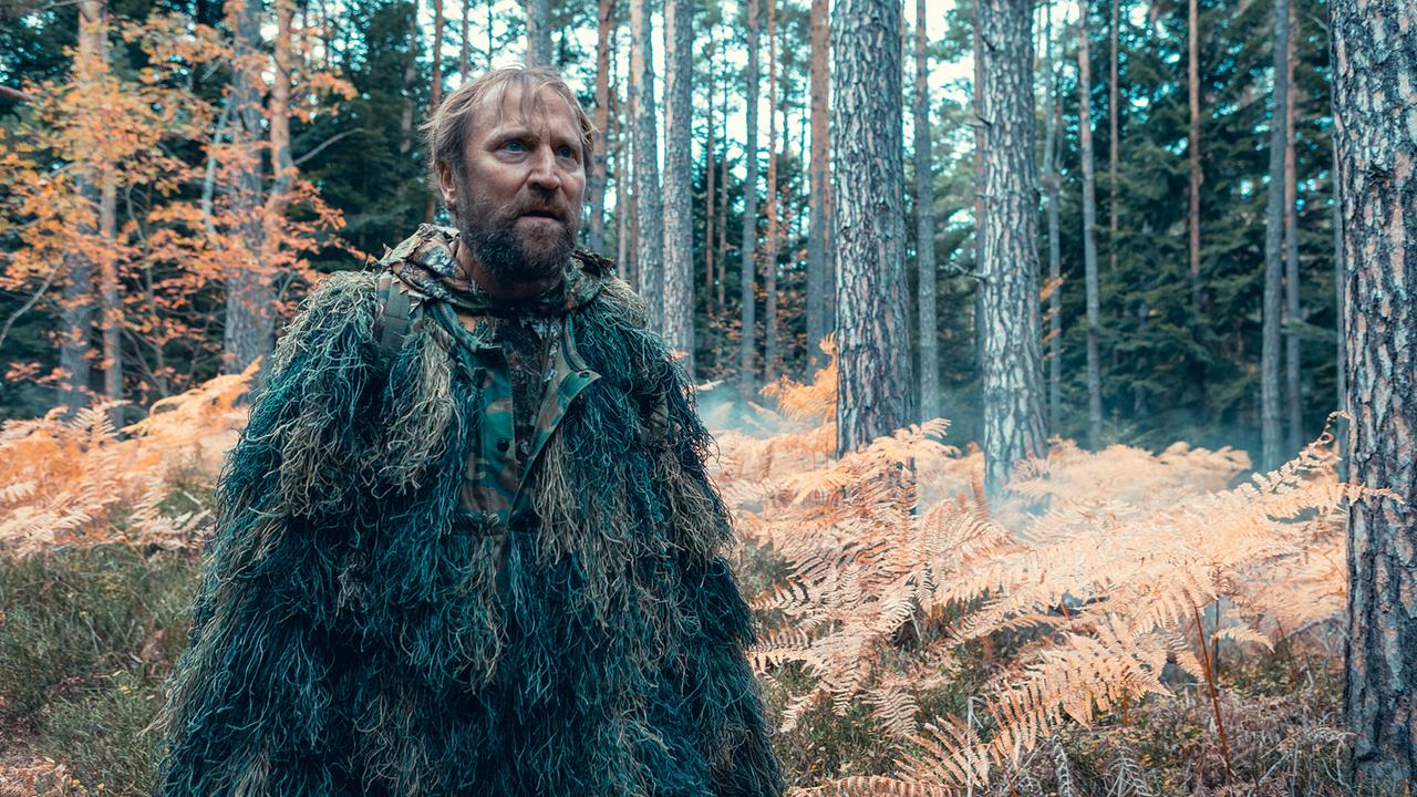 © ORF/Allegro Film/Anjeza Cikopano Norbert in Tarnkleidung steht mitten in einem herbstlichen Wald.
