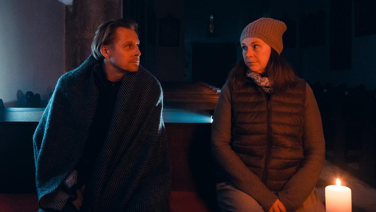© ORF/Allegro Film/Anjeza Cikopano Matias und Carola sitzen bei Kerzenschein in einer dunklen Kirche und sehen sich an.
