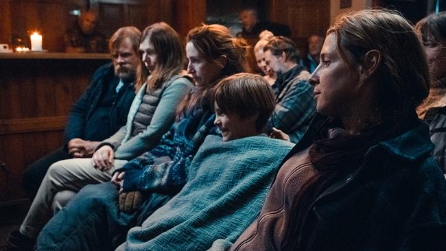Mehrere Menschen, darunter Jens, Carola, Max, Elisabeth, Bernhard und Agnes, sitzen eng beieinander in einer von Kerzen erhellten Raum.