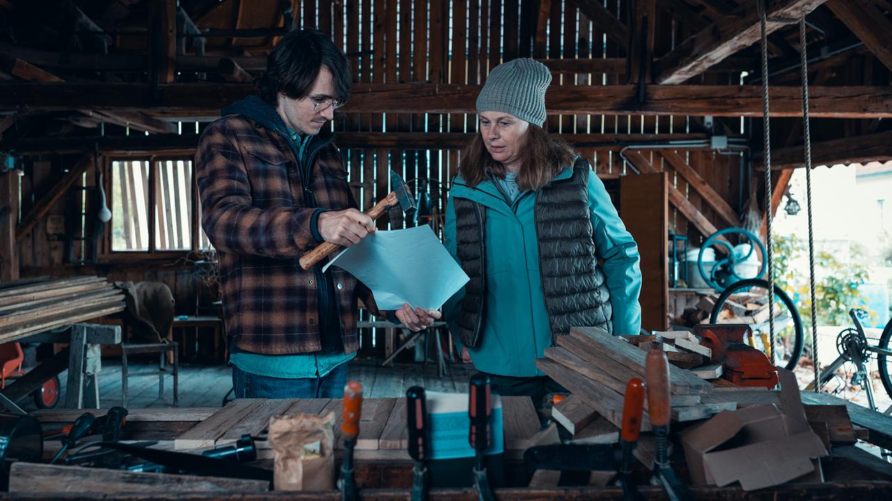 © ORF/Allegro Film/Anjeza Cikopano In einer Werkstatt zeigt Jakob mit einem Hammer in der Hand Carola ein Blatt Papier.