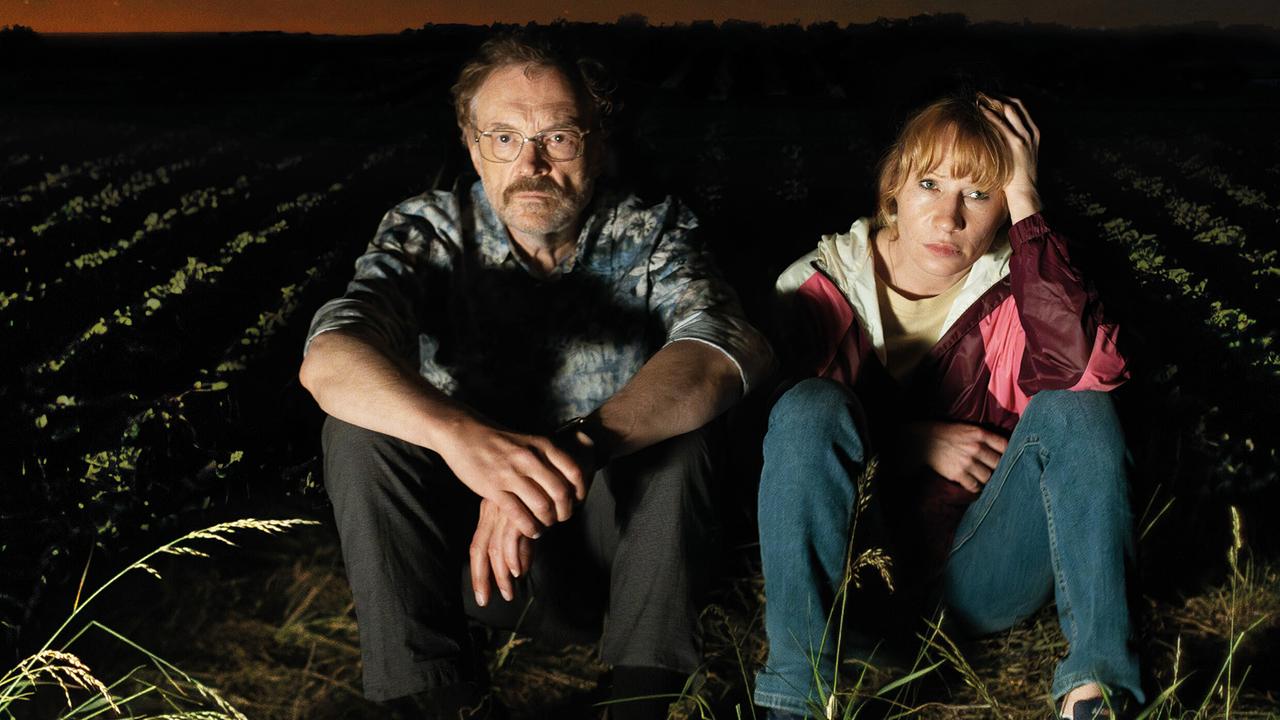 Franz und Andrea sitzen nachts ernst blickend am Rand eines Feldes unter einem sternklaren Himmel.