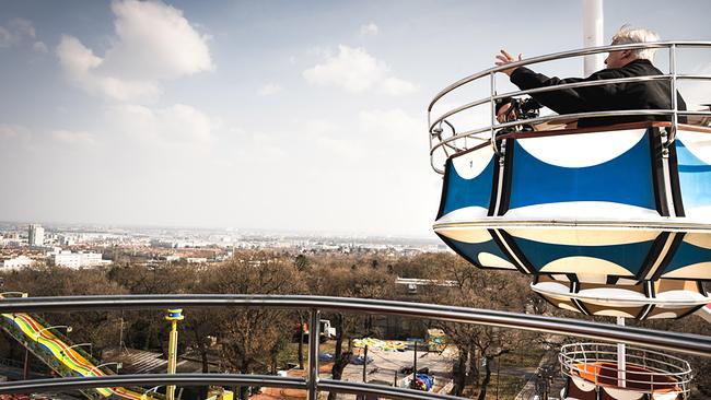 Andreas Vitásek sitzt in einer Gondel eines Riesenrad hoch über dem Prater und blickt bei hellem Himmel auf die Stadtlandschaft in der Ferne.