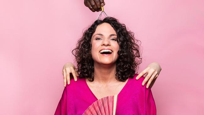 © ORF/Agentur Sobieszek/Jasmin Schuller Antonia Stabinger sitzt lächelnd vor rosa Hintergrund, während mehrere Hände von außen sie mit einem Fächer, einer Kopfmassage-Spinne und einer Berührung an den Schultern verwöhnen.