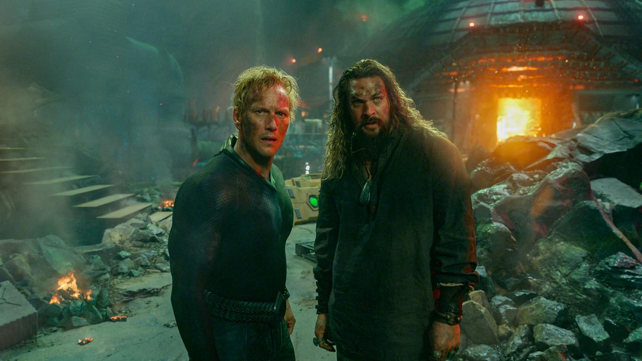 Zwei Männer stehen in einer zerstörten, rauchgefüllten Umgebung, im Hintergrund lodert ein Feuer in einem Kuppelgebäude