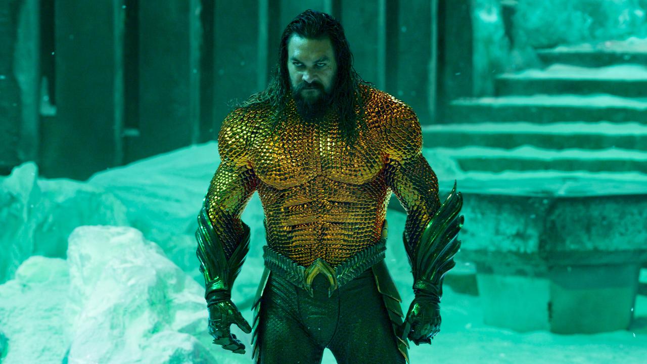 Jason Momoa als Aquaman in goldgrüner, schuppenartiger Rüstung steht in türkis beleuchteter Umgebung mit Treppen im HIntergrund