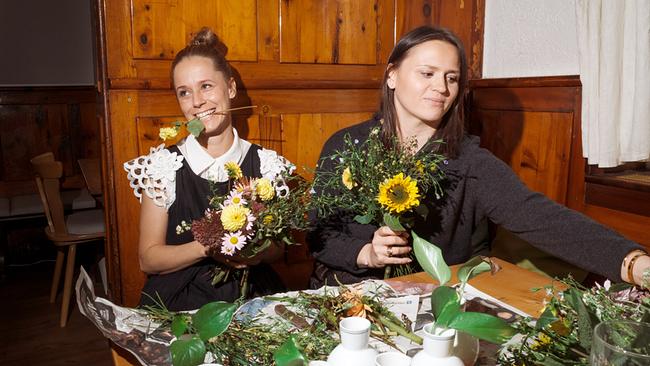 © ORF/Jenseide OG/Robert Oberzaucher Kira Saskia Schinko mit Marie Rahofer sitzen im berühmten Linzer Leopoldistüberl an einem Holztisch und binden bunte Blumensträuße, während vor ihnen Vasen und Pflanzenreste liegen.