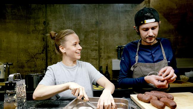 Kira Schinko mit Sternekoch Harald Irka bereiten in einer Küche Lebensmittel zu, wobei Kira etwas schneidet und  Harald Irka Würste formt.