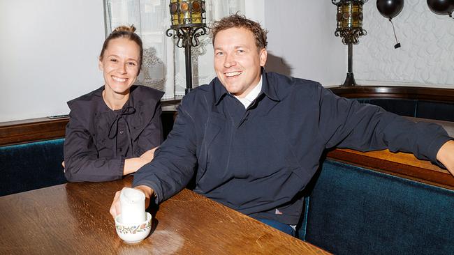 Kira Schinko mit Sternekoch Philipp Rachinger sitzen lächelnd in einer gemütlichen Gaststube an einem Holztisch, vor ihnen eine Kerze.