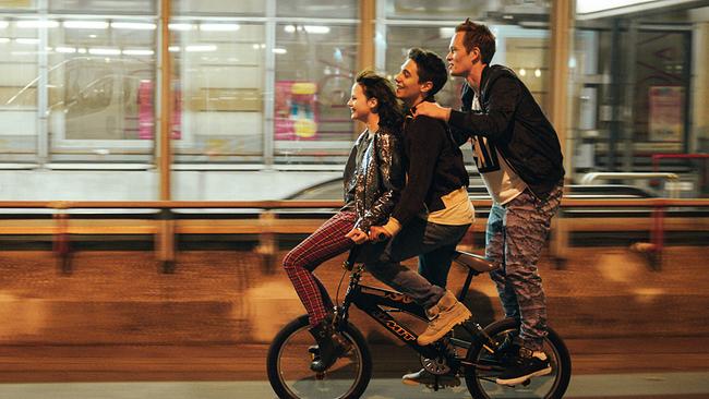Die drei Jugendlichen Charly, Carlo und Sulzer fahren auf einem kleinen Fahrrad durch eine nächtlich beleuchtete Straße.