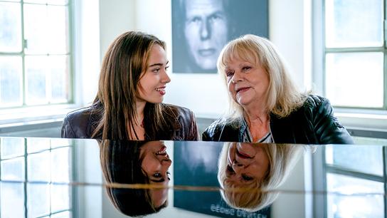 Mara Romei und Marianne Mendt gemeinsam am Klavier, im Hintergrund ein Bild von Georg Danzer