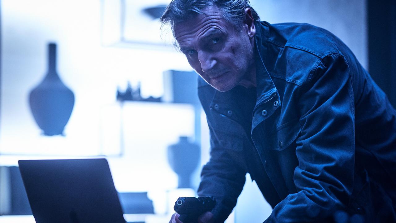 © ORF/Wild Bunch/Ben King Liam Neeson als Travis Block, angespannt blickt er mit gezückter Waffe nach vorne, während er die andere Hand an der Tastatur eines Laptops hält