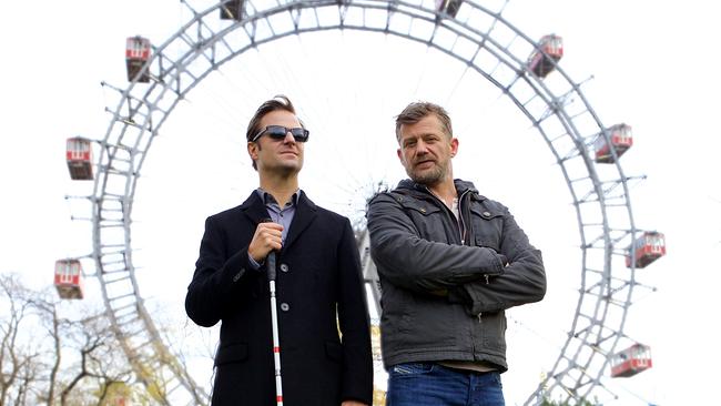 © ORF/Mona Film/Philipp Brozsek Philipp Hochmair als Alex Haller mit dunkler Sonnenbrille und Blindenstock mit Andreas Guenther als Nikolai Falk auf der Wiese vor dem Wiener Risenrad