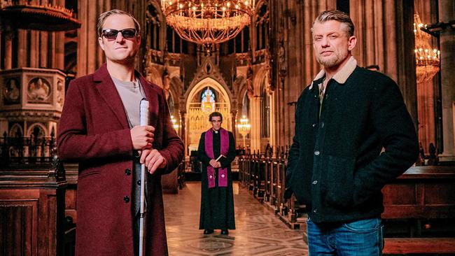 © ORF/Mona Film/ Tivoli Film/Philipp Brozsek Philipp Hochmair als Alexander Haller mit dunkler Brille und Blindenstock und Andreas Guenther als Nikolai Falk stehen in der Kirche, hinter ihnen im Gang zwischen den Bänken steht ein Pfarrer, im Hintergrund der Altar