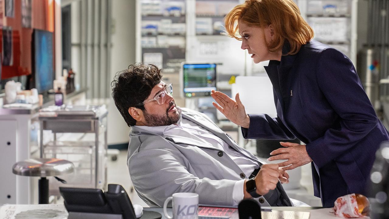 © ORF/Warner Bros. Pictures Susan Sarandon als Victoria Kord in Lederjacke bedroht Harvey Guillén als Dr. Sanchez, der an seinem Schreibtisch sitzt und vor ihrer Drohung zurückweicht
