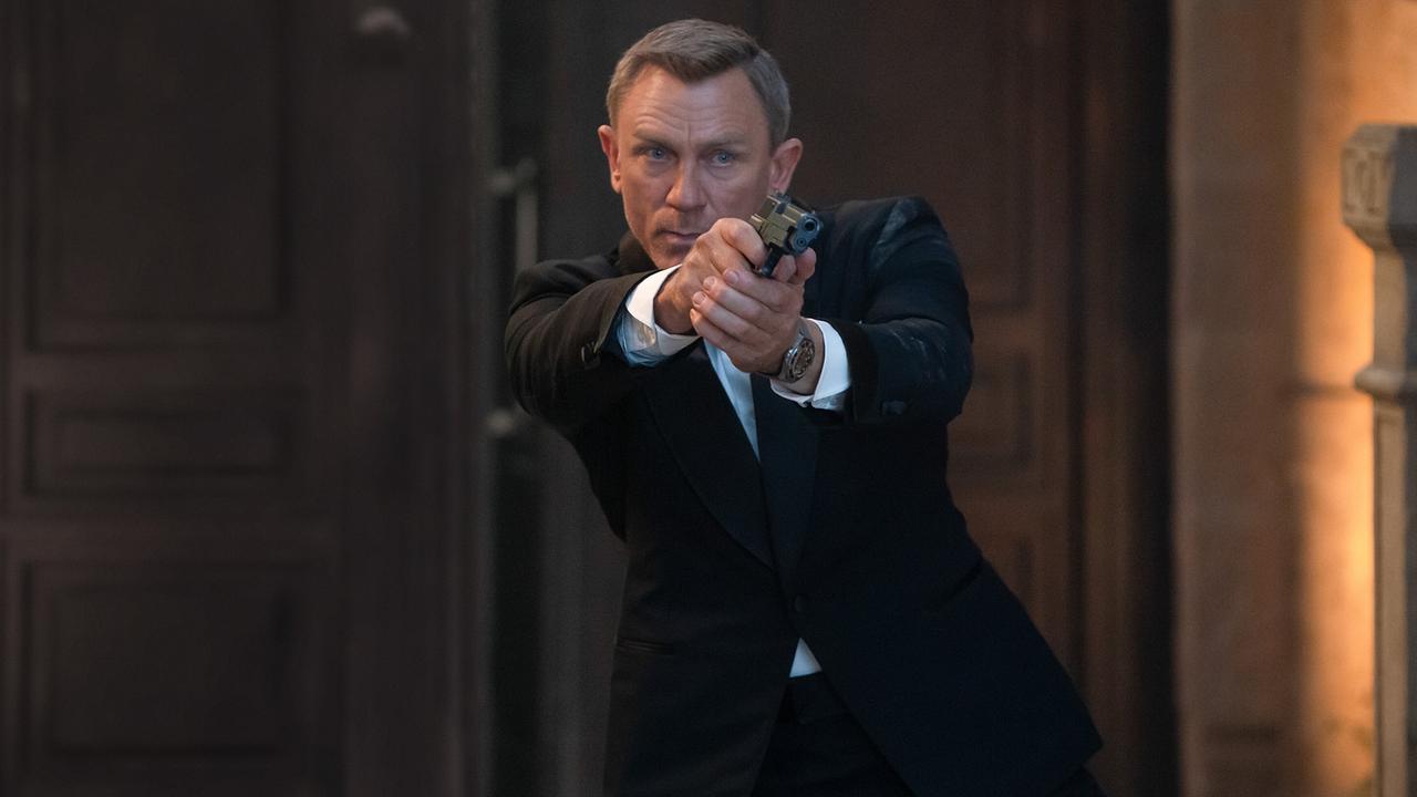 Daniel Craig als James Bond, im Smoking steht er in einem Vorhaus und hält mit beiden Händen seine Pistole im Anschlag