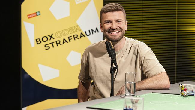 Thomas Seidl sitzt im Studio an einem Tisch mit einem kleinen Modell-Fußballfeld und Figuren darauf vor einem „Box oder Strafraum“-Hintergrund.