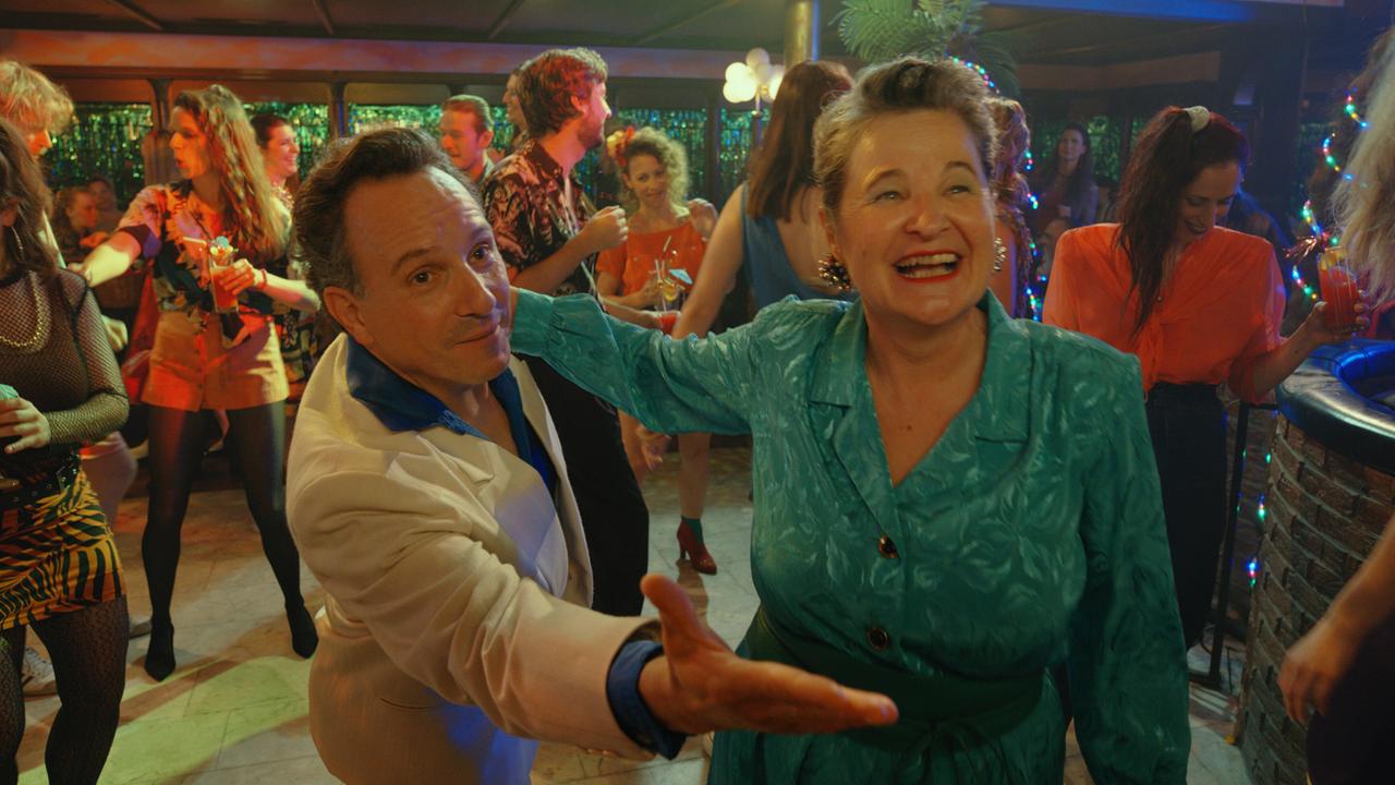 Helfried und Herta Tschach tanzen lachend auf einer vollen Tanzfläche in einem farbenfrohen Lokal.