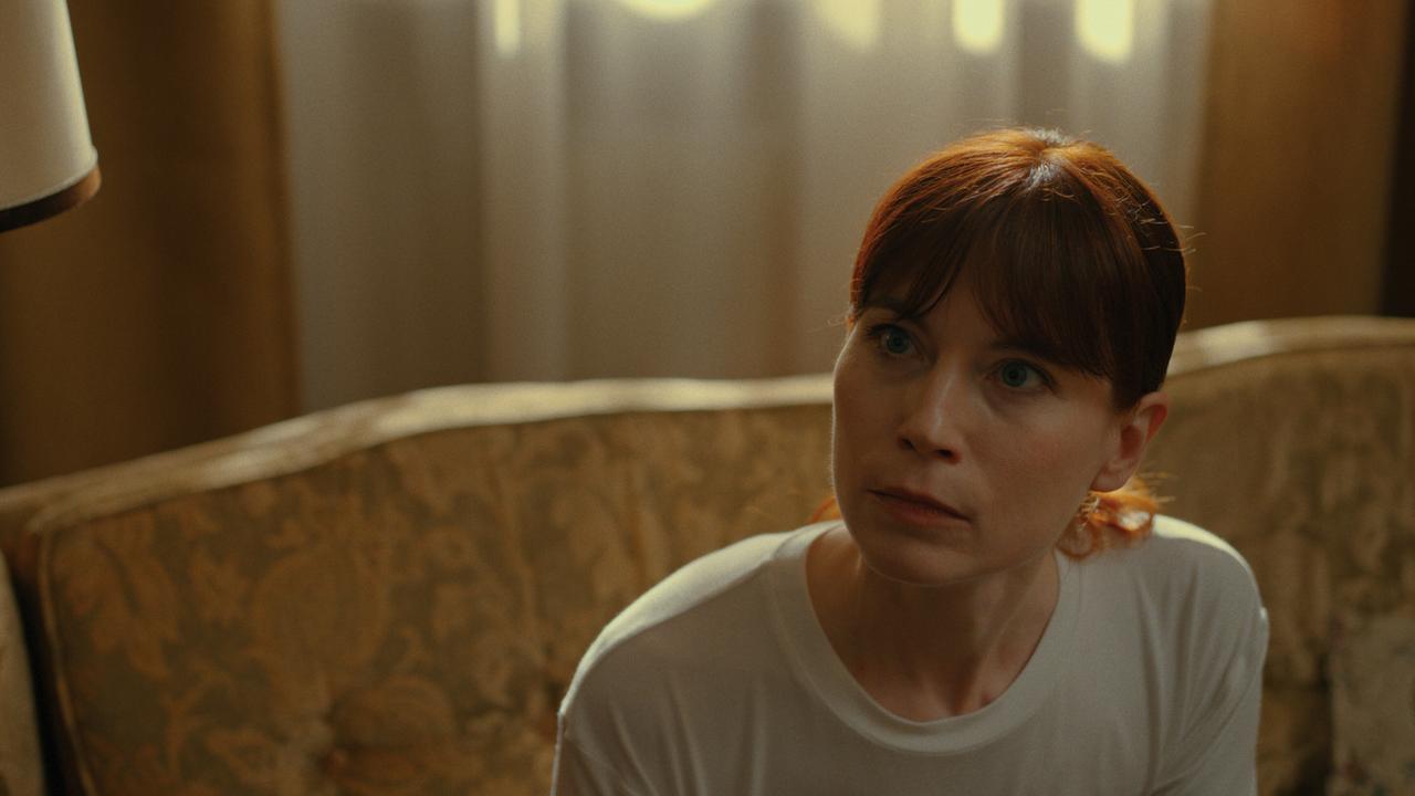  Deborah Feist sitzt auf einem Sofa in einem warm beleuchteten Raum.