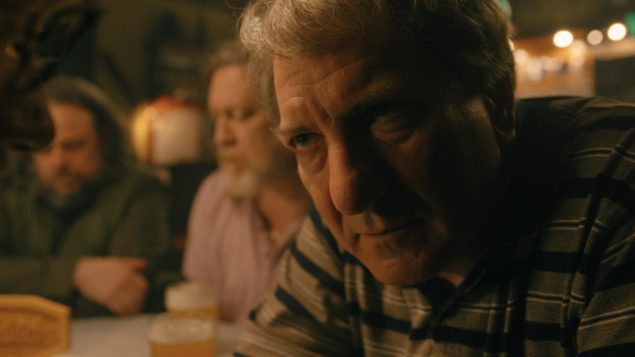 Gerri Tschach im Vordergrund sitzt mit weiteren Männern an einem Tisch in einer Gaststube mit Biergläsern.