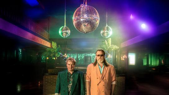 Gerri Tschach und Richard Pfeisinger, beide im 80er-Jahre-Outfit, stehen allein auf einer leeren Tanzfläche unter Discokugeln in einem Club.