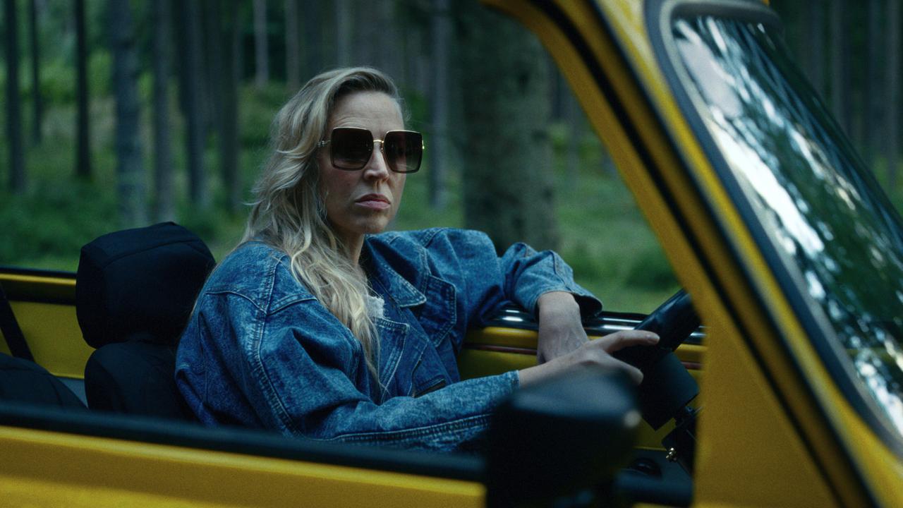 © ORF/Superfilm Elfi Pfeisinger fährt mit einem gelben Cabrio durch einen Wald.