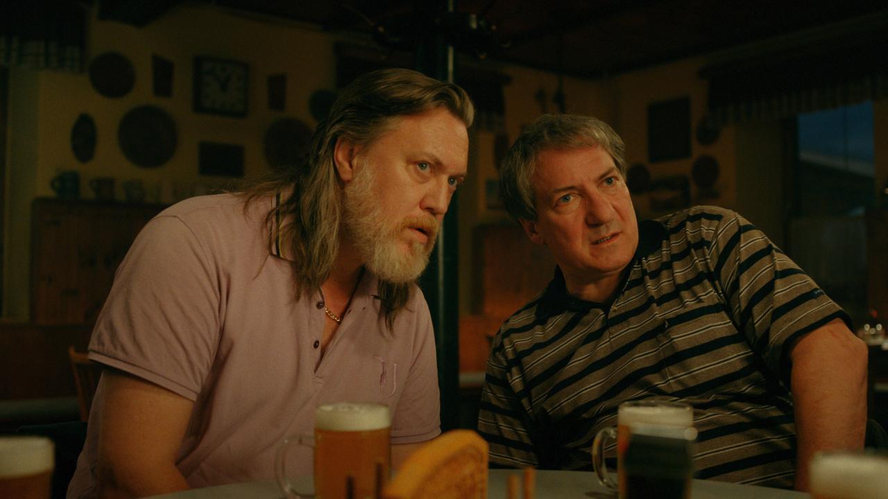 © ORF/Superfilm Richard Pfeisinger und Gerri Tschach sitzen in einem Wirtshaus vor Biergläsern und beugen sich vertraulich zueinander.