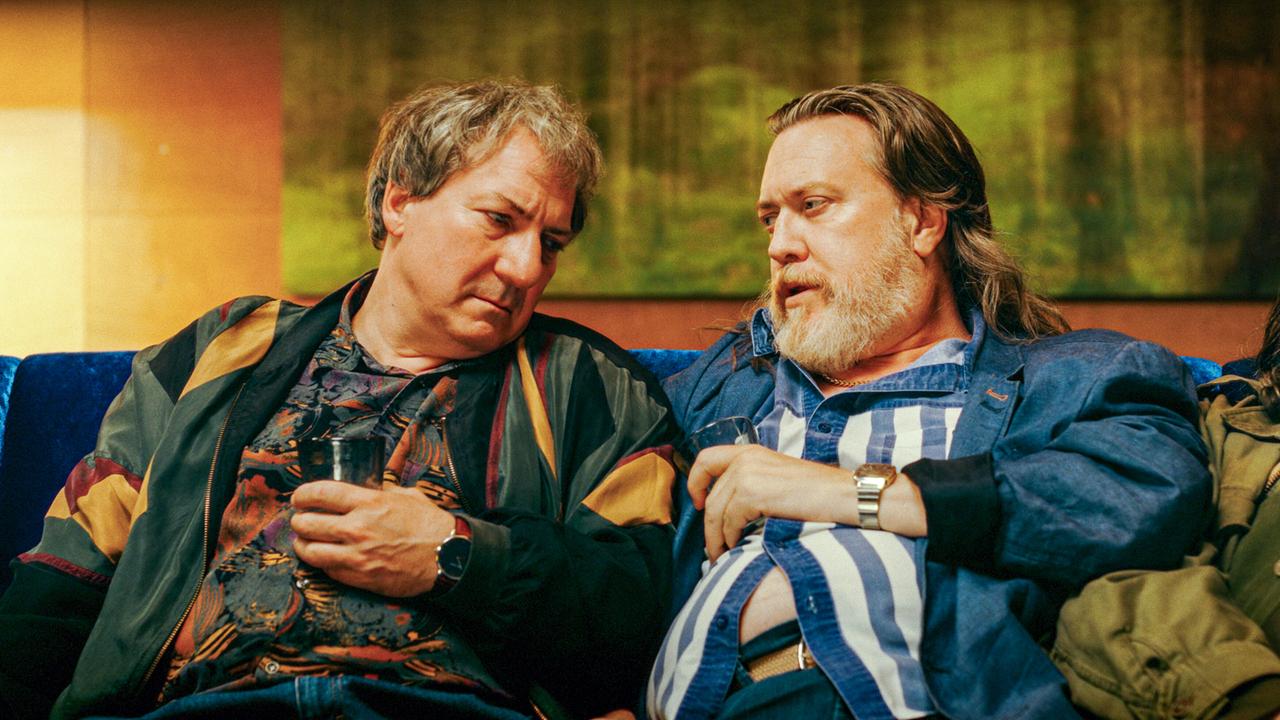 Gerri Tschach und Richard Pfeisinger sitzen nebeneinander auf einem Sofa in einem Innenraum mit einem Waldbild im Hintergrund.