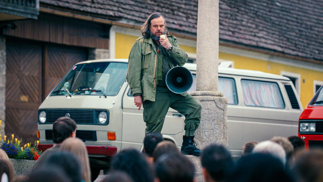 Reinhard Matussek steht erhöht im Freien und spricht mit einem Megafon zu einer versammelten Menschenmenge.