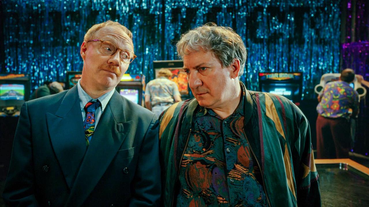 Katzlbrunner und Gerri Tschach stehen vor Spielautomaten in einer bunt beleuchteten Spielhalle.