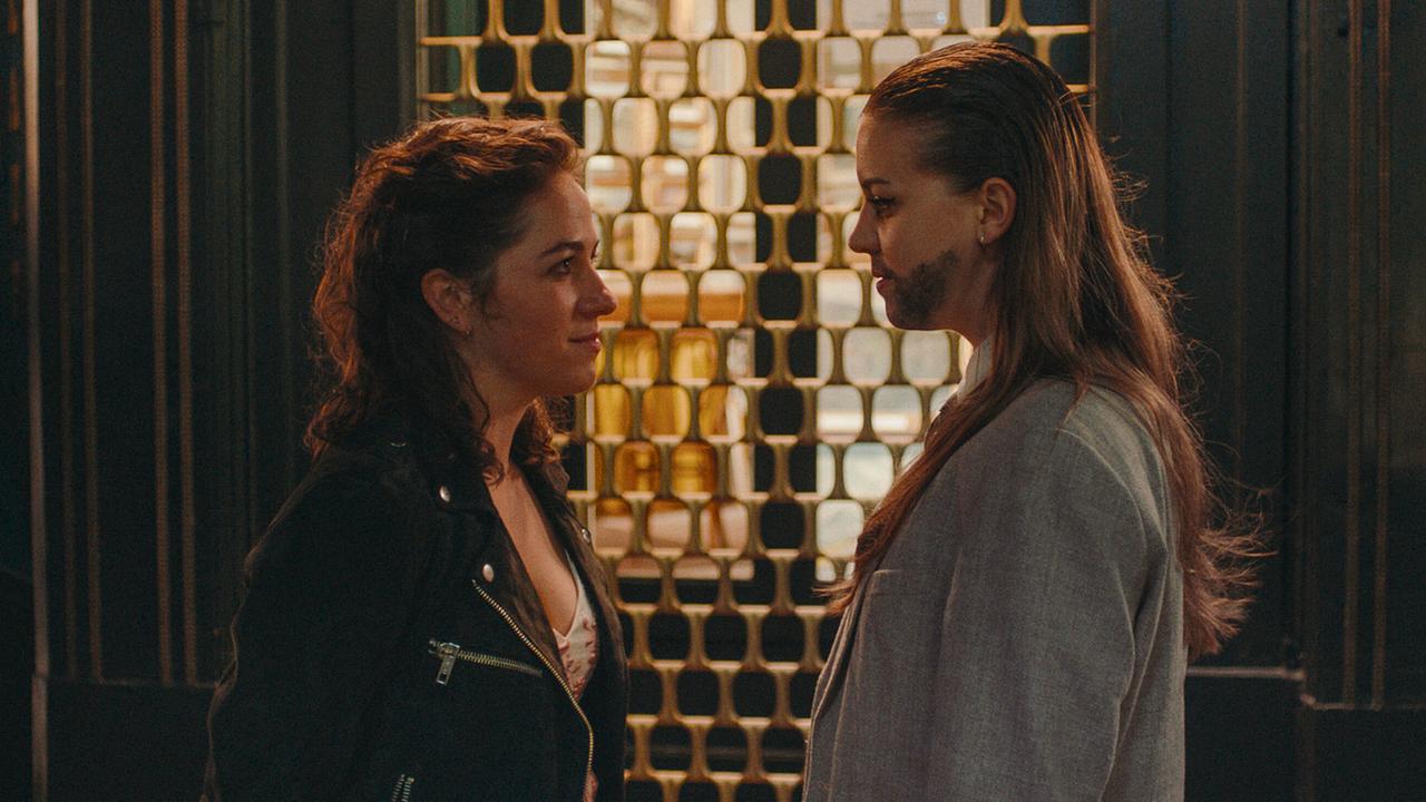 Theresa und Mira stehen einander in einem stilvoll beleuchteten Eingangsbereich gegenüber.