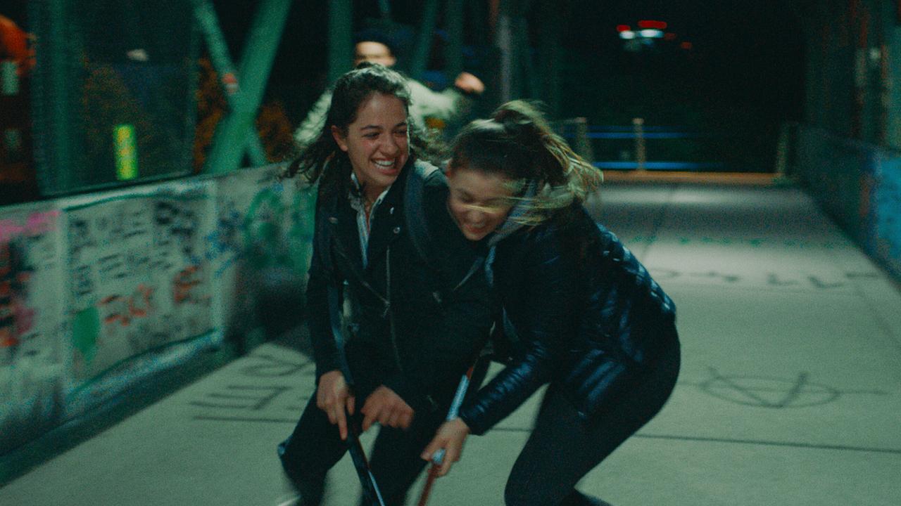 Theresa und Mira stehen lachend mit Stöcken auf einer bunt besprühten Brücke.