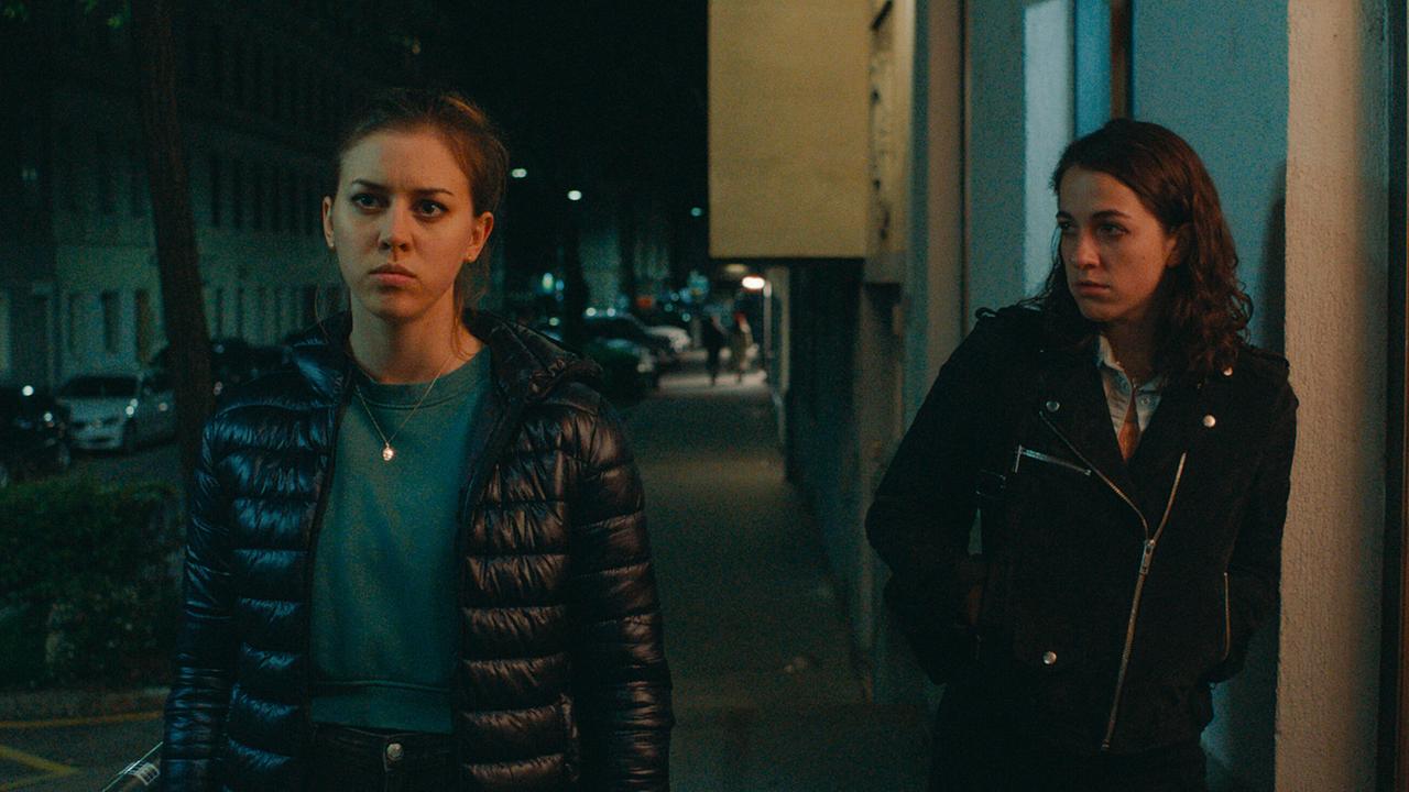 Mira und Theresa gehen nachts durch eine beleuchtete Straße.