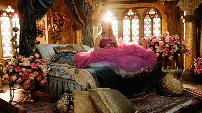 Jella Haase in einem reich geschmückten Schlafzimmer eines Märchenschlosses, zwischen riesigen Blumensträußen sitzt sie in einem rosaroten Kleid auf ihrem Bett
